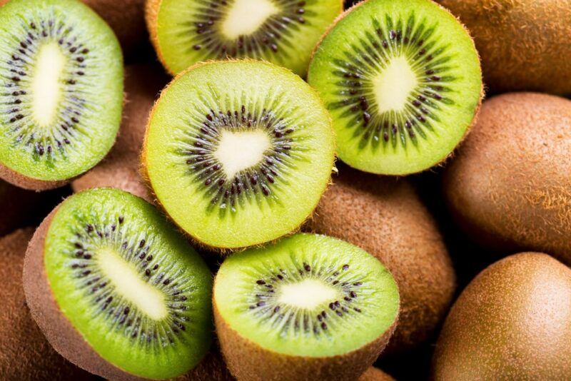 A pile of fresh kiwis, some of which have been cut in half