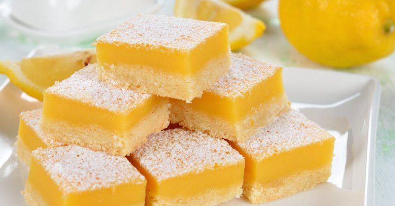 Various lemon bars cut up in a pile with powdered sugar