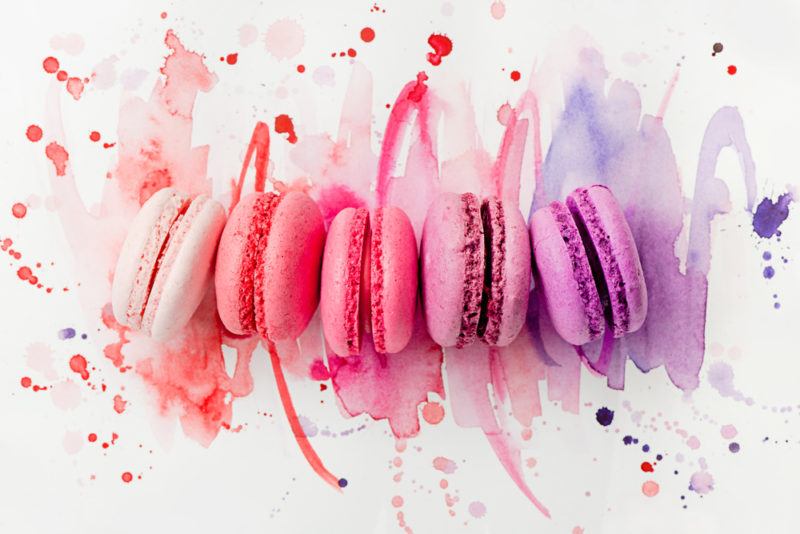 Five macarons in different colors with colored paint underneath them