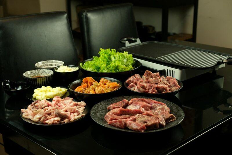 Black dishes of meat and veggies, with a black griddle and grill combo