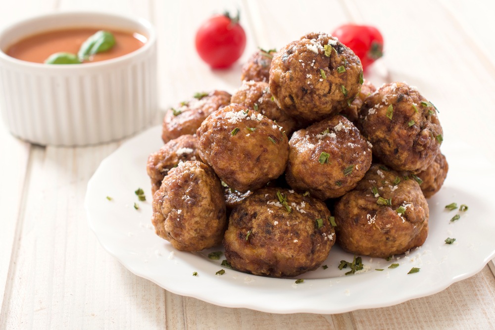 A white dish of meatballs piled high, with a dish of sauce in the background