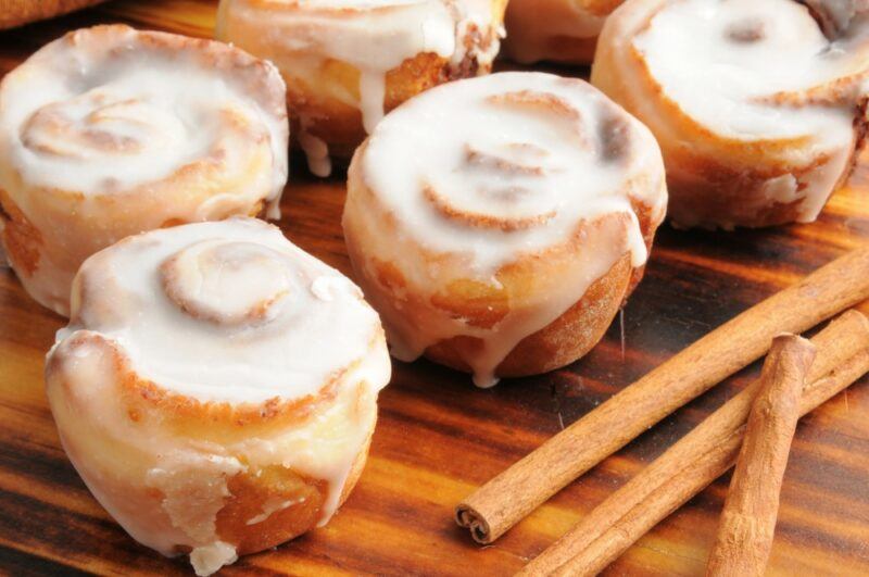 A selection of mini cinnamon buns with icing, next to some cinnamon sticks