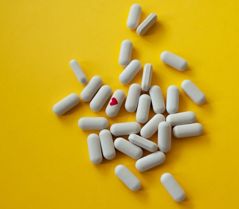 A bright yellow background with a variety of multivitamins, one of which has a red heart on it