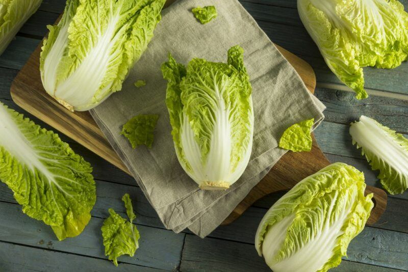 A top down image of five or six napa cabbage heads on a wooden table.