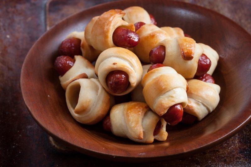 A brown dish of pigs in blankets on a wooden table