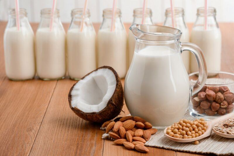 A line of bottles of milk, with a jug of milk in front and various nuts and seeds, suggesting the idea of plant-based milk