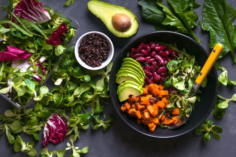 A black bowl with a quinoa salad and fresh greens