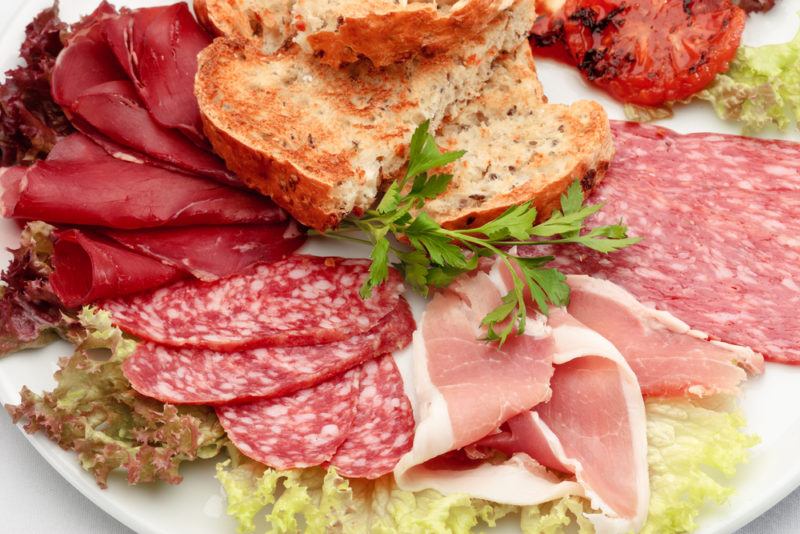 Sliced cold cut meats on a white dish with greens and bread