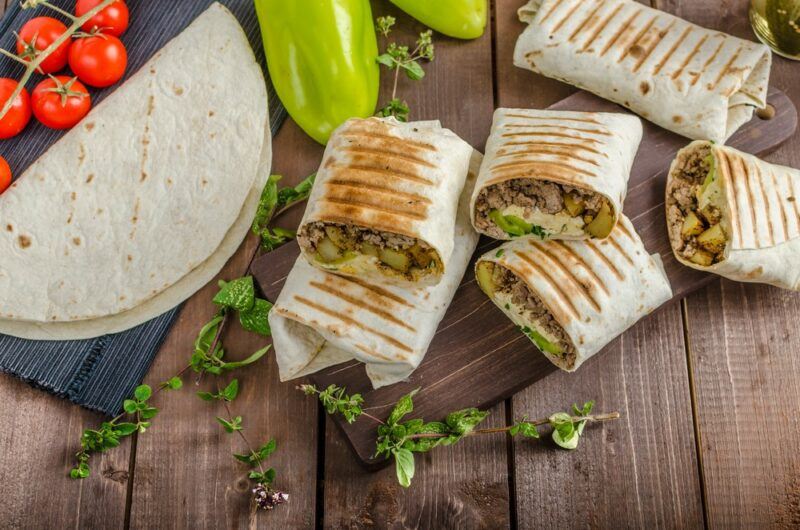 A wooden table with six small breakfast burritos