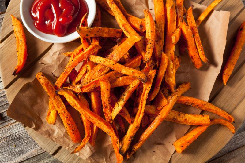 Many sweet potato fries on a piece of paper next to sauce