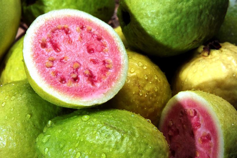 A selection of whole guava with one cut open revealing the pink interior