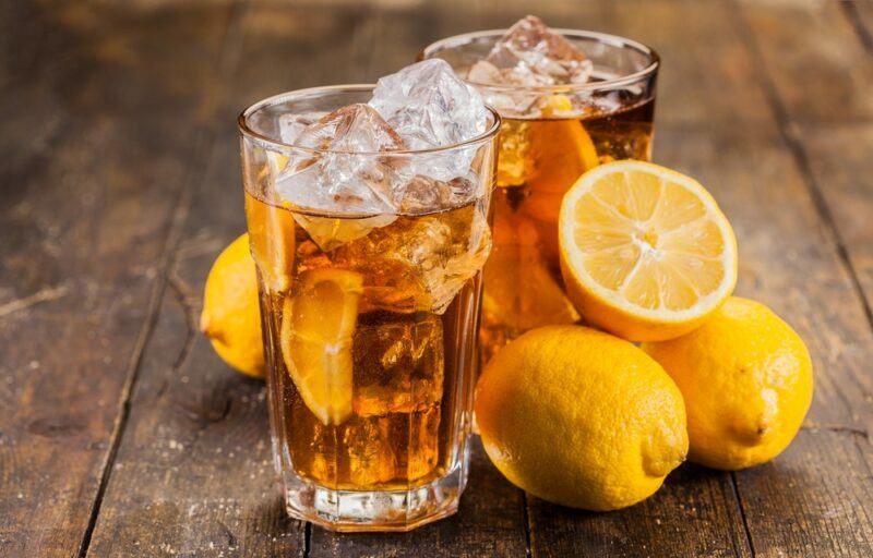 Two large glasses with ice, containing a senor root beer cocktail, next to fresh lemons