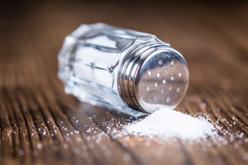 A salt shaker that's been tipped over on a table, spilling iodized salt