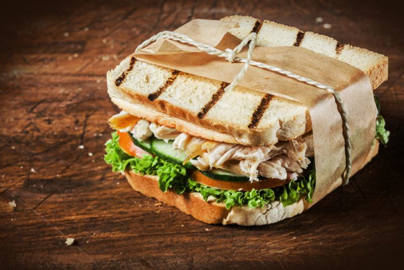 A toasted sandwich wrapped in paper on a wooden table that contains chicken and vegetables