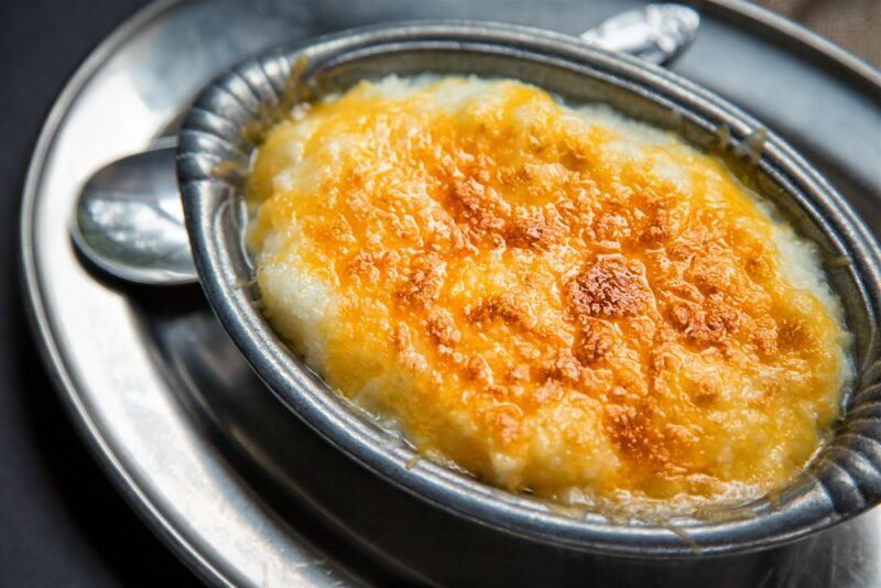 A silver dish containing grits covered with cheese