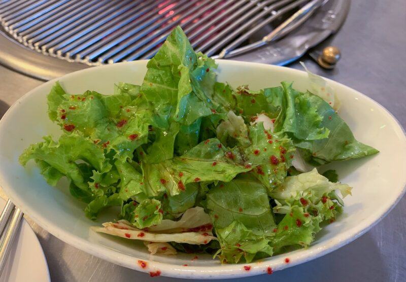 A shallow white dish containing a simple Korean lettuce salad with spices as part of the seasoning.