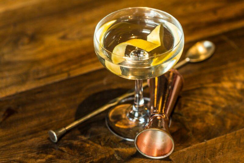 A wooden table with a single moonshine martini next to a cocktail jigger and a stirring spoon