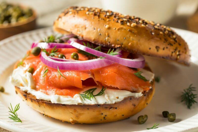 A single bagel on a plate, filled with cream cheese, salmon, and red onions