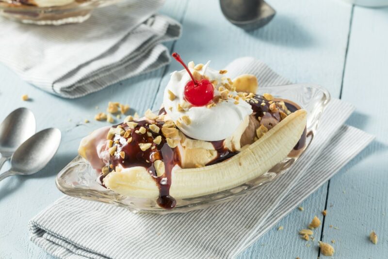 A cloth on a light blue table with a banana split that's loaded with ice cream, cream, and nuts