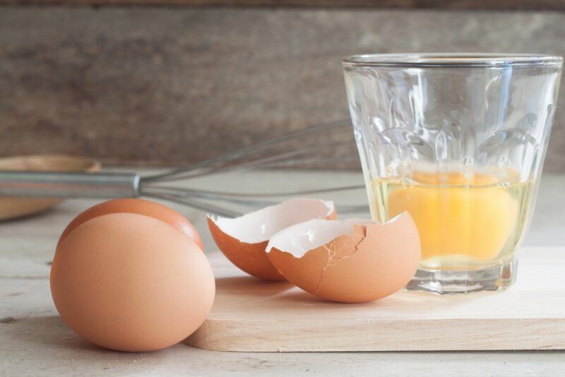 A single raw egg that's been broken into a glass, next to egg shells and two whole eggs