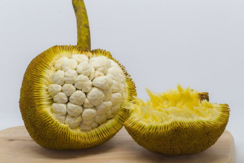 A marang fruit on a table, where some of the skin has been peeled off to show a white interior