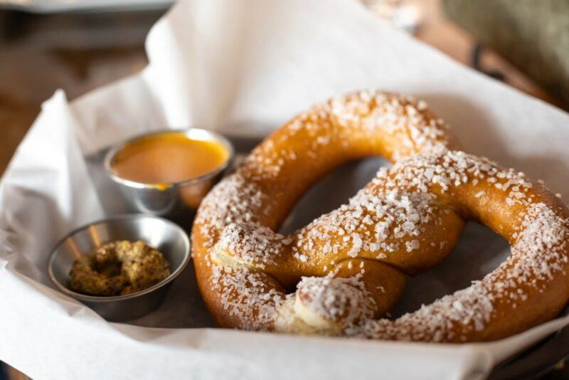 A single large pretzel in parchment paper, next to two small containers of mustard