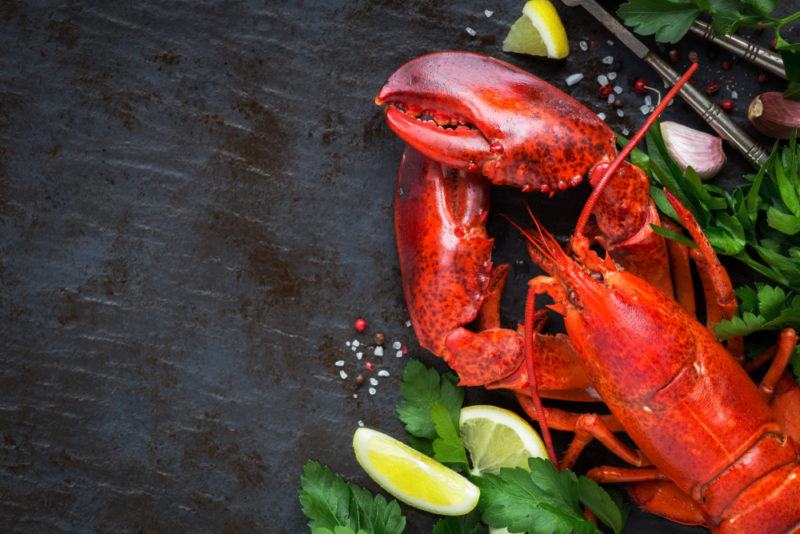 A lobster in the bottom right of the image with some greenery, seasoning, amd lemon wedges