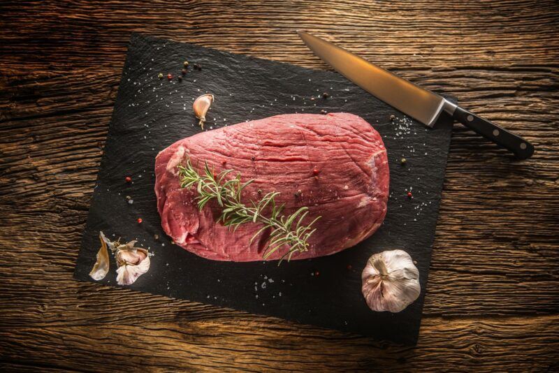 A black slate board on a table with some garlic and a knife