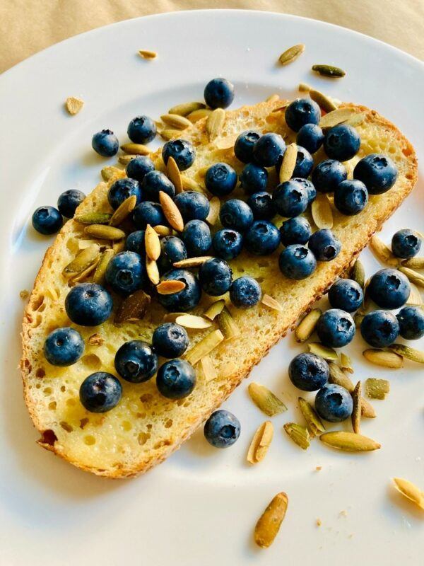 A slice of sourdough with blueberries and pumpkin seeds on a white plate