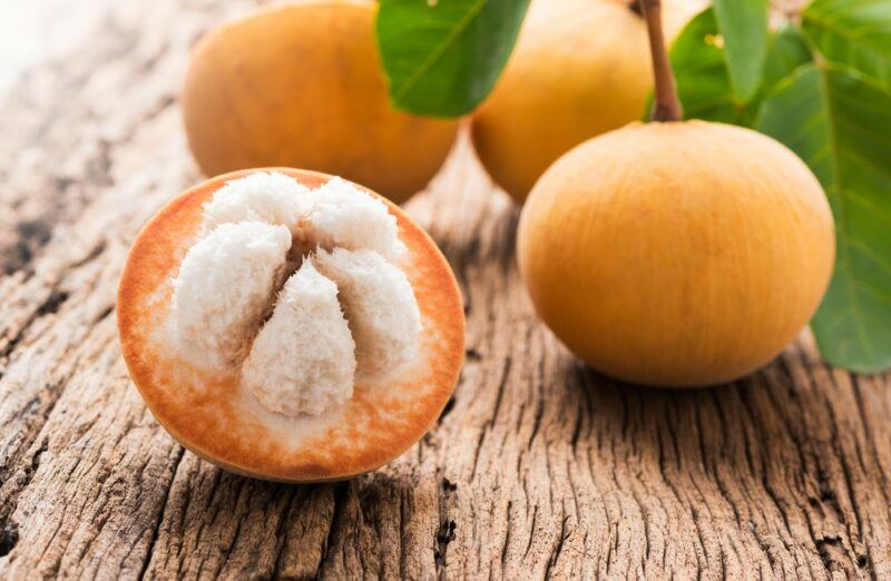 A wooden table with half a santol fruit that's been cut open and a few whole fruit in the background