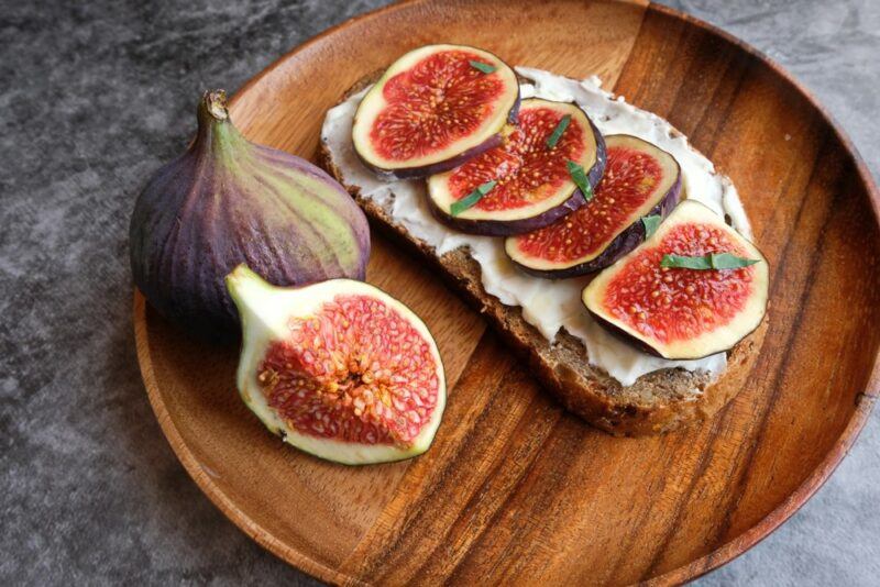 A single slice of sourdough with a yogurt and feta spread that's been topped with sliced figs, with a full fig and part of a fig next to it