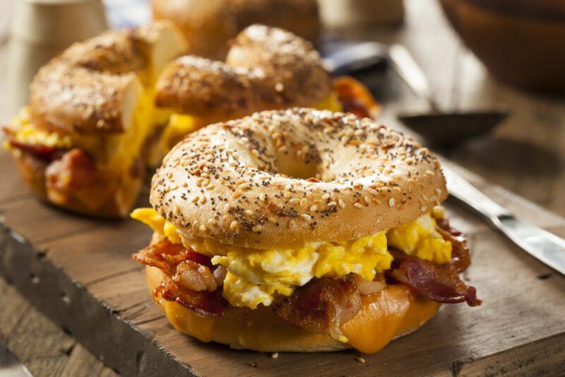 A wooden board with two breakfast bagels that are filled with bacon and egg