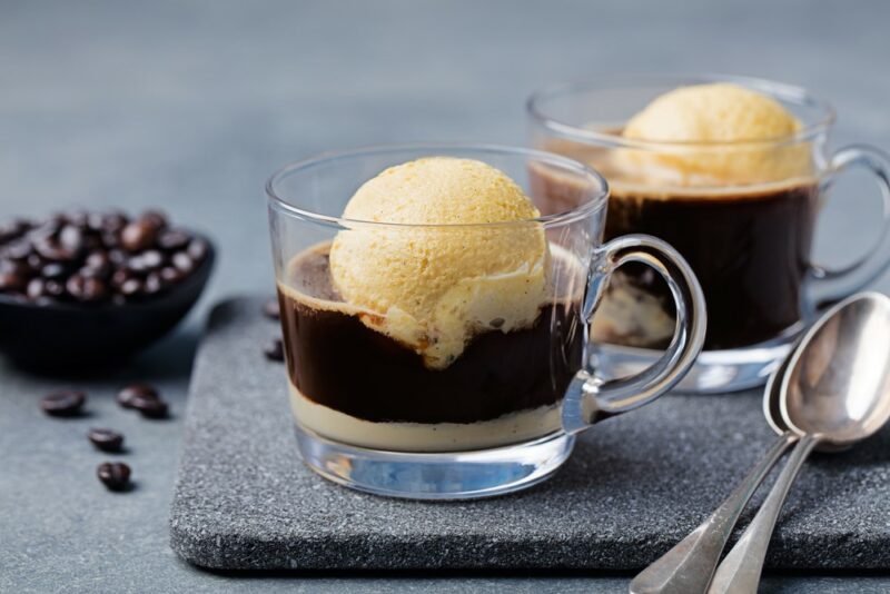 Two glass mugs containing affogato desserts, each with a scoop of vanilla ice cream, with some coffee beans in the background