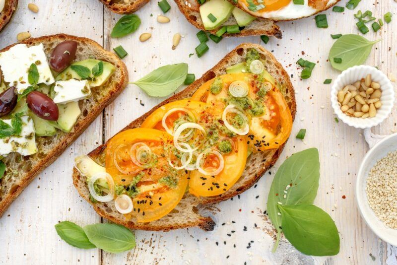 Two slices of sourdough. One has pesto, yellow tomatoes, and onions, while the second has feta and olives