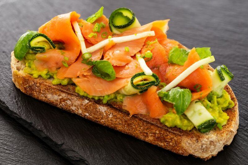 A single piece of sourdough with smoked salmon, avocado, and zucchini