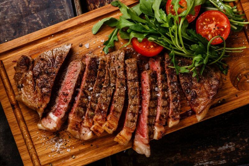 A wooden board with steak that has been sliced into small pieces, with lettuce and tomatoes