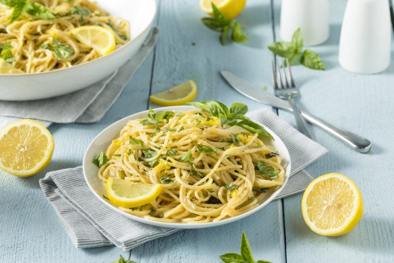 A white bowl and a white plate with lemon pasta on a blue table