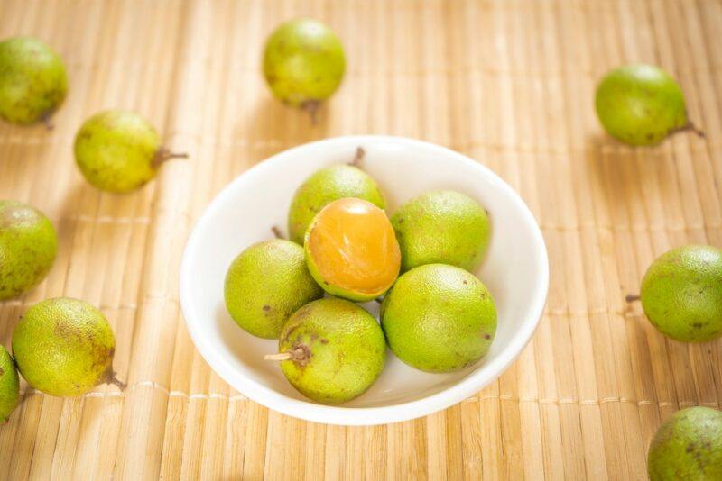 A light wooden table that's scattered with genips and Spanish limes, with a white bowl containing even more of the fruit