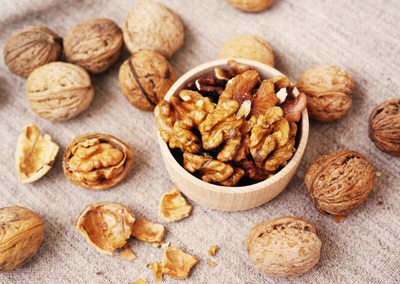 A small wooden dowl with walnut halves, surrounded by walnuts