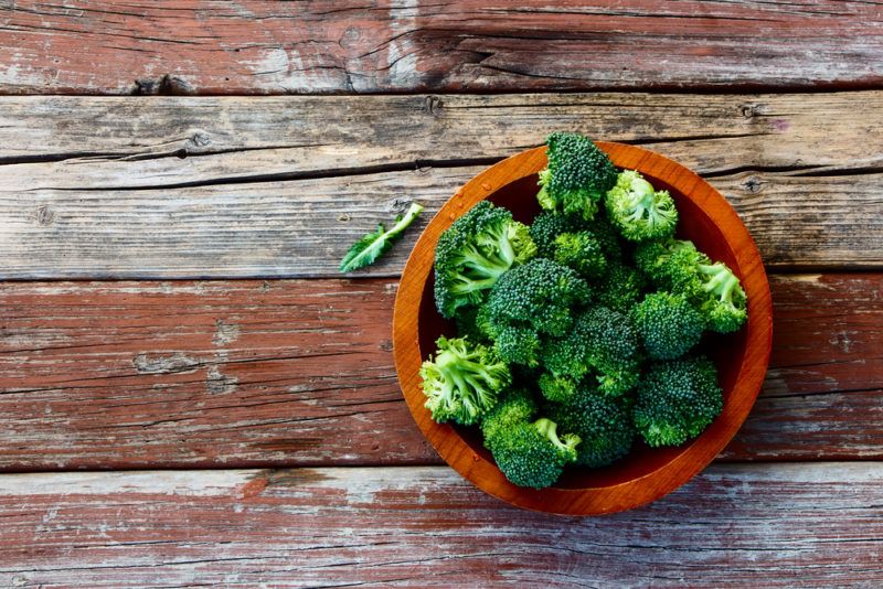 A small brown red bowl filled with broccoli on a wooden deck or floor