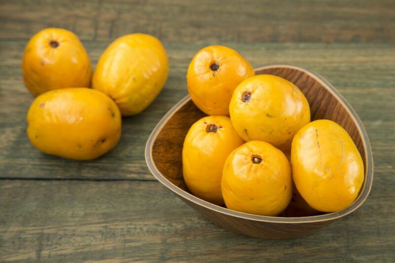 A small bowl of yellow ciruela fruit, next to three more on a wooden table