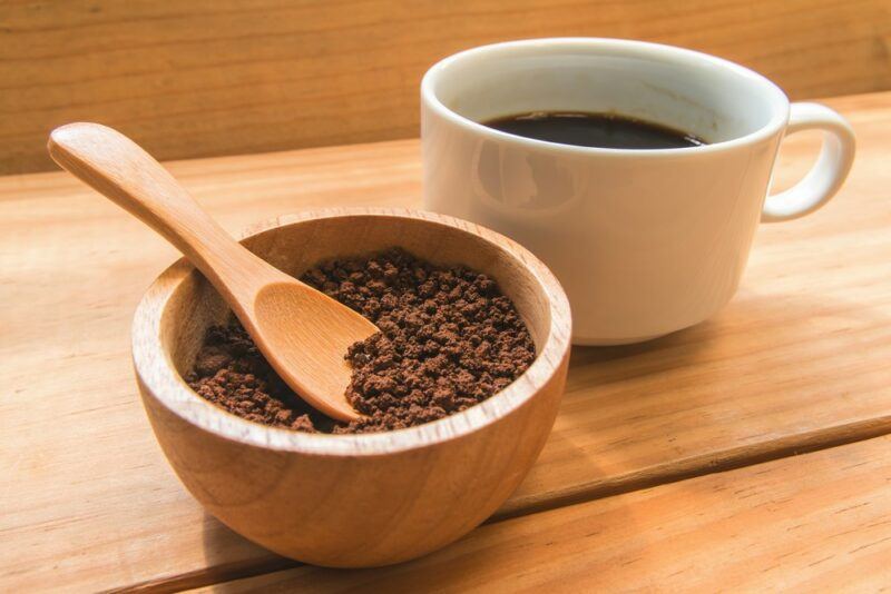 A brown wooden bowl with instant Nestle coffee next to a white mug of hot coffee