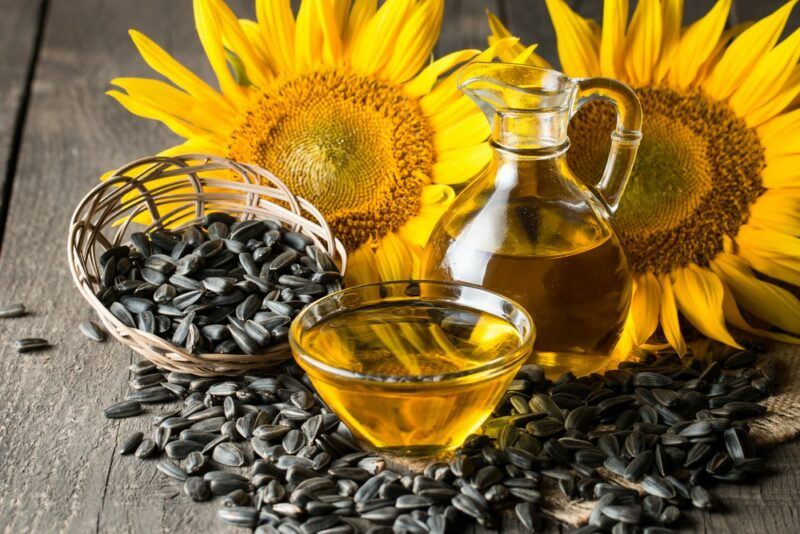 A glass bottle and dish of sunflower oil, next to a basket of sunflower seeds and some sunflowers