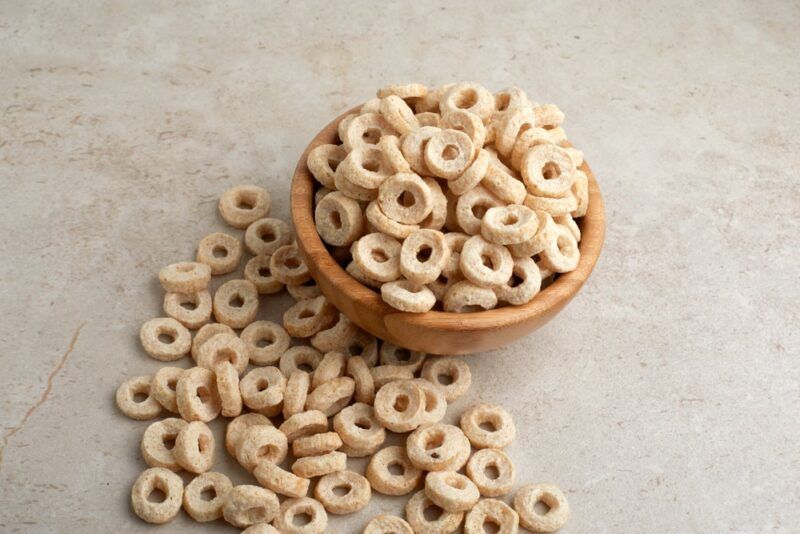 A small brown bowl containing Cheerios, with more Cheerios on the table under it