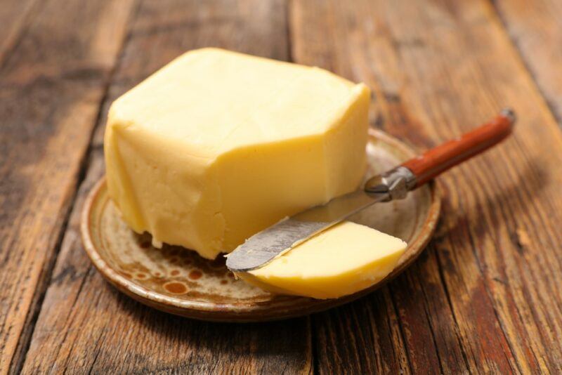 A block of butter with a piece cut using a knife, on a small brown plate on a wooden table