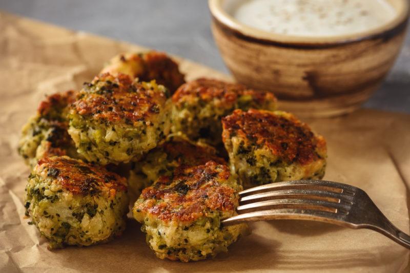 A plate filled with broccoli balls next to a bowl of dip