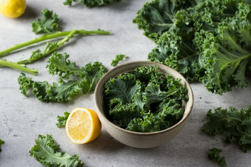 A small bowl of curly kale, next to half a lemon, with more kale around it