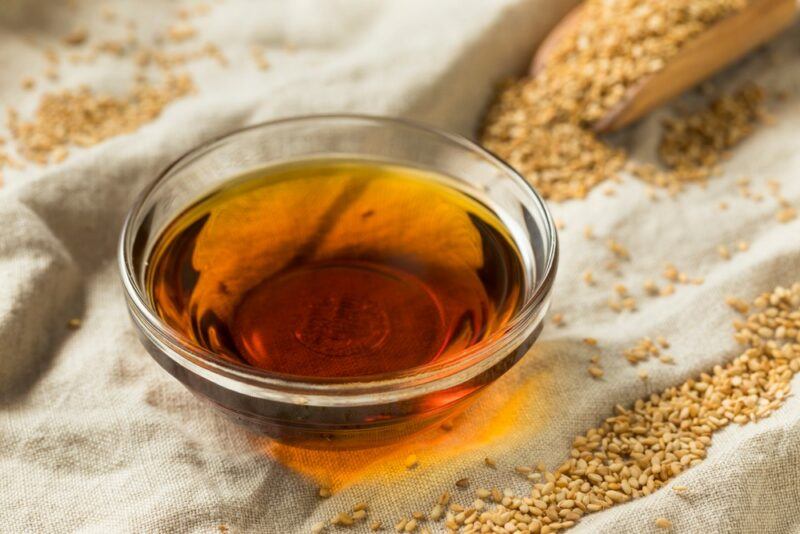 A glass dish of sesame seed oil, with sesame seeds scattered around it