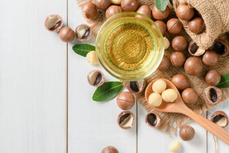 A white table with various macadamia nuts, some unshelled macadamia nuts and some macadamia nut oil