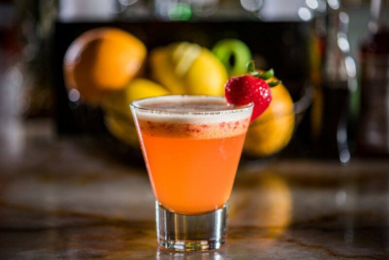 A small glass of a white madras cocktail, in front of a bowl of fruit